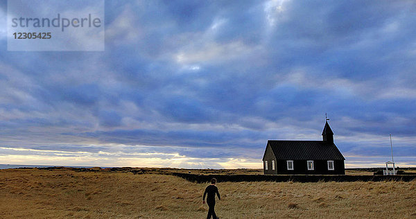 Stimmungsvoller Sonnenuntergangshimmel über einer Person  die in Richtung Kirche im Reykholt-Tal  Island  läuft