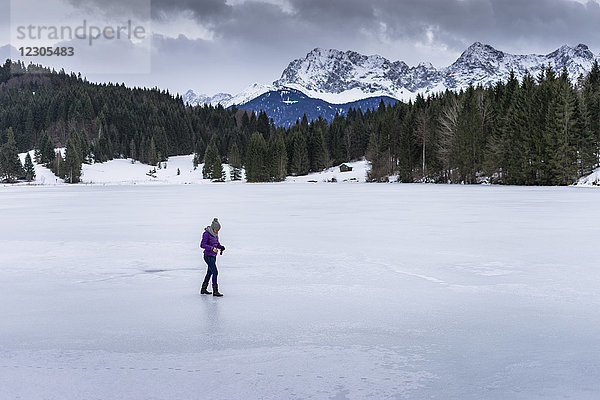 Seitenansicht einer Frau  die im Winter auf einem zugefrorenen See in den bayerischen Alpen spazieren geht  Garmisch-Partenkirchen  Bayern  Deutschland