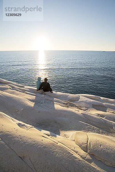 Rückansicht eines Paares mit Blick auf das Meer  während es auf der Klippe Scala dei Turchi sitzt  Sizilien  Italien