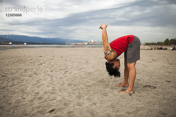 Mann dehnt sich vor Acroyoga am Strand