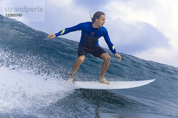 Junger Mann reitet auf einem Surfbrett auf einer Welle im Meer