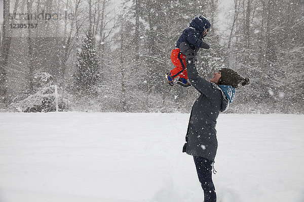 Mutter hält ihren kleinen Sohn beim Spielen im Freien im Winter hoch