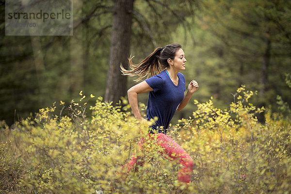 Seitenansicht einer jungen sportlichen Frau beim Trailrunning im Wald