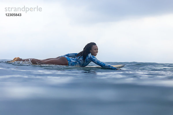 Seitenansicht einer Frau  die auf einem Surfbrett im Meer paddelt