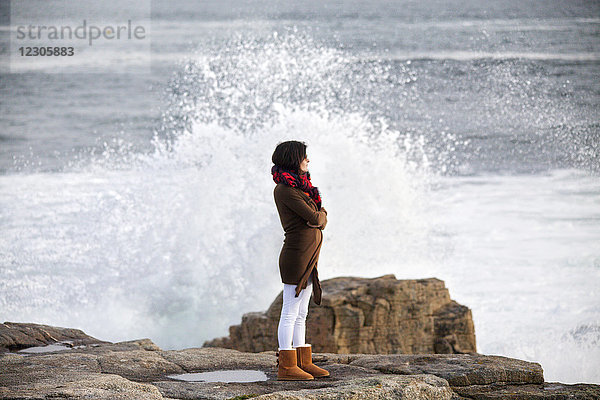 Seitenansicht einer Frau  die an einer felsigen Küste steht  hinter der die Wellen brechen