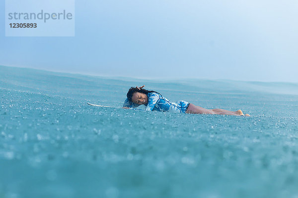 Lächelnde Frau auf Surfbrett im Meer liegend