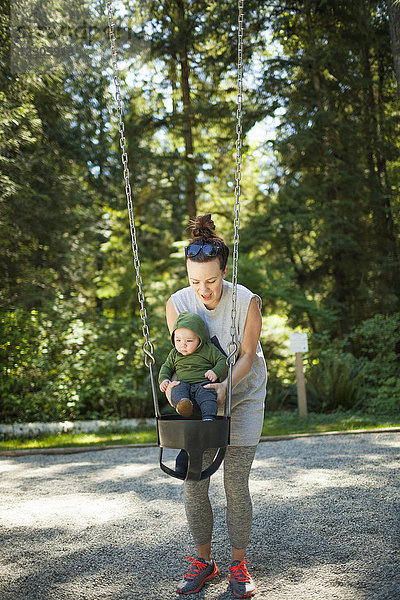 Vorderansicht einer Mutter mit ihrem kleinen Sohn  der auf einer Schaukel im Park spielt