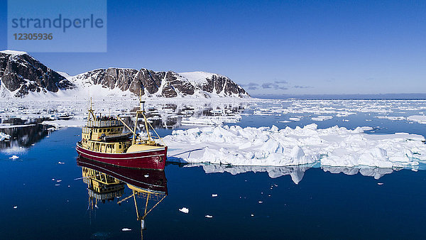 Fischerboot im arktischen Meer mit Packeis und felsigen Bergen im Hintergrund  Raudfjorden  Spitzbergen  Svalbard und Jan Mayen  Norwegen