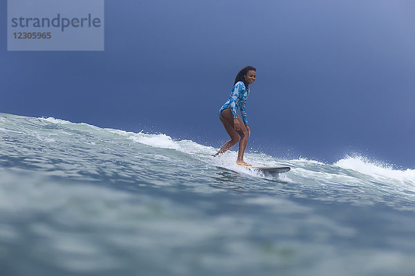 Totale Aufnahme einer einzelnen Frau  die auf einem Surfbrett im Meer auf einer Welle reitet