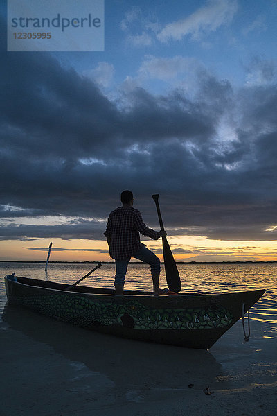 Silhouette eines Mannes  der in einem Kanu steht und ein Paddel am Meeresufer hält  Cancun  Quintana Roo  Mexiko