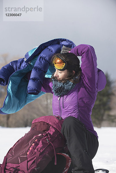 Foto einer alleinstehenden Frau  die im Winter im Freien eine warme Winterjacke anzieht