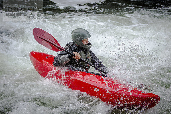 Wildwasserkajakfahrer paddelt durch einen turbulenten Fluss