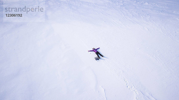 Luftaufnahme einer alleinstehenden Frau  die im Winter im Freien einen Schneeengel macht