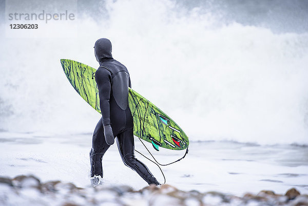 Surfer im Neoprenanzug mit Surfbrett und Spaziergang im Meer