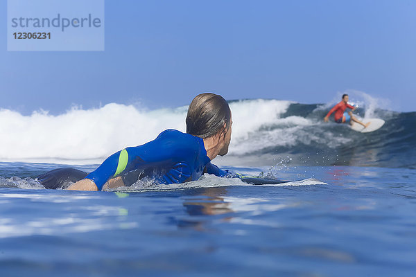 Junger Mann paddelt auf einem Surfbrett im Meer