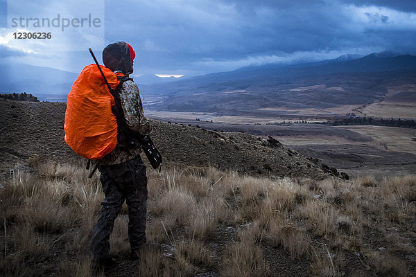 Hirschjäger geht mit Gewehr durch das Hinterland von Colorado bei Sonnenaufgang  während sich ein Gewitter nähert  Colorado  Colorado  USA