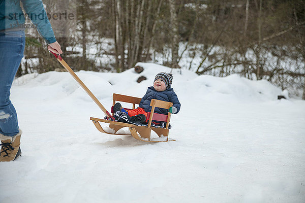 Mutter spielt im Winter mit ihrem Sohn im Freien  indem sie ihn auf einem Schlitten zieht