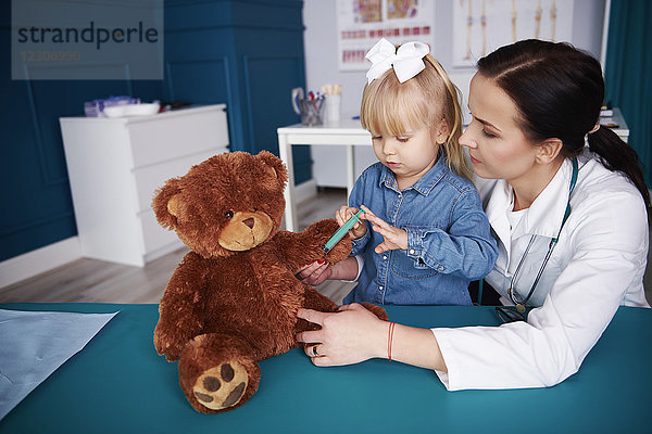 Arzt und Mädchen impfen Teddy in der Arztpraxis
