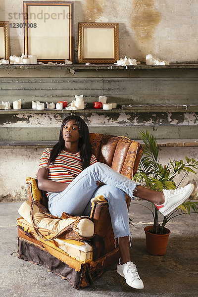 Porträt einer coolen jungen Frau  die auf einem alten Lederstuhl im Loft sitzt.