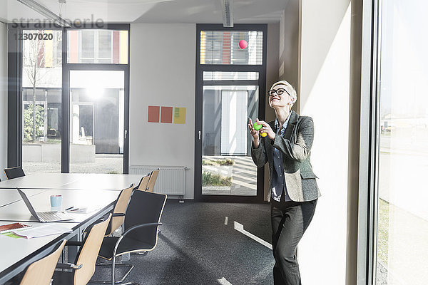 Lächelnde Geschäftsfrau jongliert mit Bällen im Büro