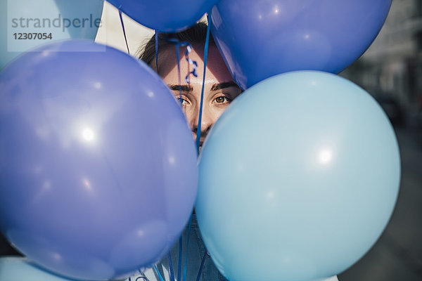 Frau versteckt sich hinter blauen Luftballons