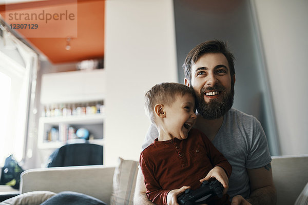 Vater und Sohn sitzen zusammen auf der Couch und spielen ein Computerspiel.
