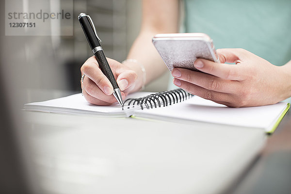 Frau schreibt Notizen im Tagebuch  hält ein Smartphone in der Hand