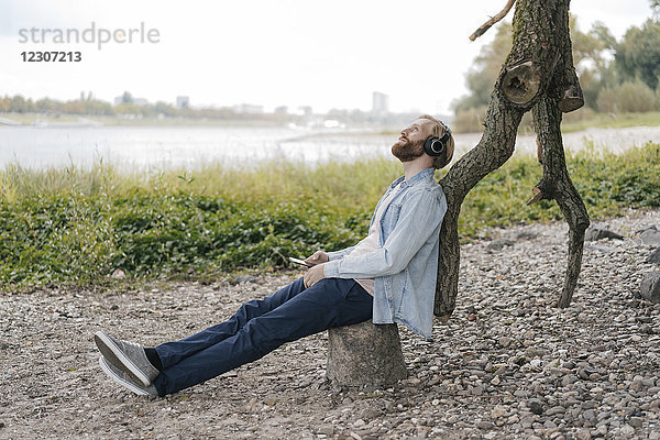 Deutschland  Düsseldorf  Mann mit Smartphone und Kopfhörer Musik hören in der Natur