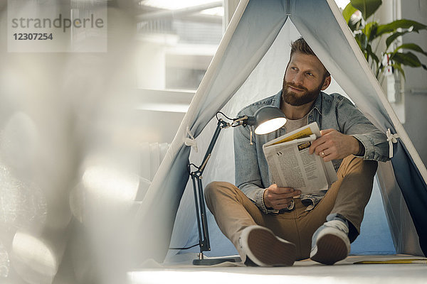 Ein Mann kampiert in seinem Wohnzimmer und liest die Zeitung.