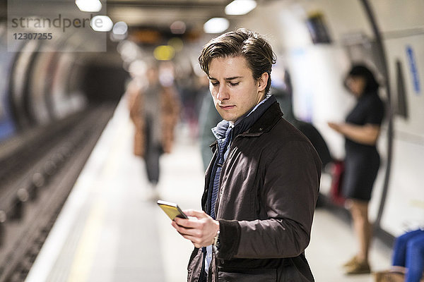 UK  London  Geschäftsmann wartet in der U-Bahn-Station mit Handy