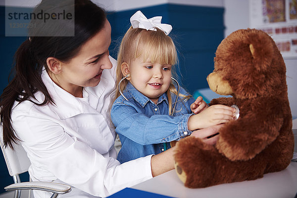 Arzt und Mädchen untersuchen Teddy in der Arztpraxis