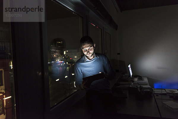Geschäftsmann sitzt nachts auf der Fensterbank im Büro mit Tablette