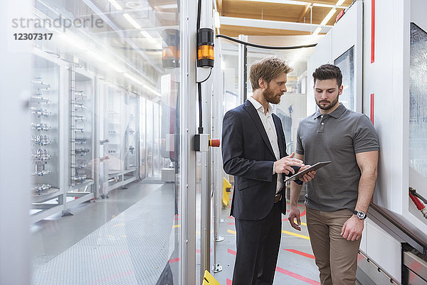 Zwei Männer mit Tablette reden an der Maschine in der modernen Fabrik