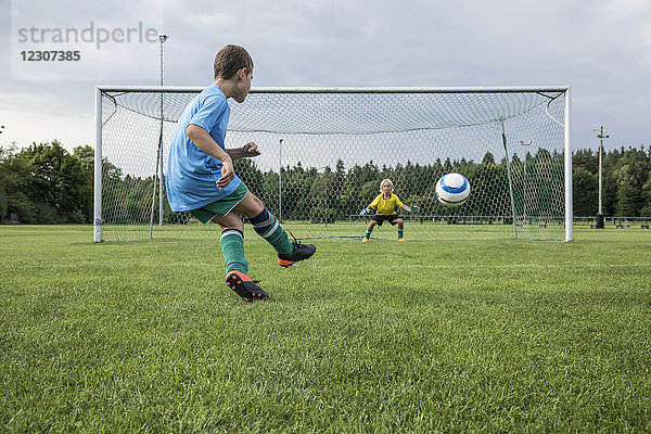 Junger Fußballspieler kickt Ball vor dem Tor mit Torhüter
