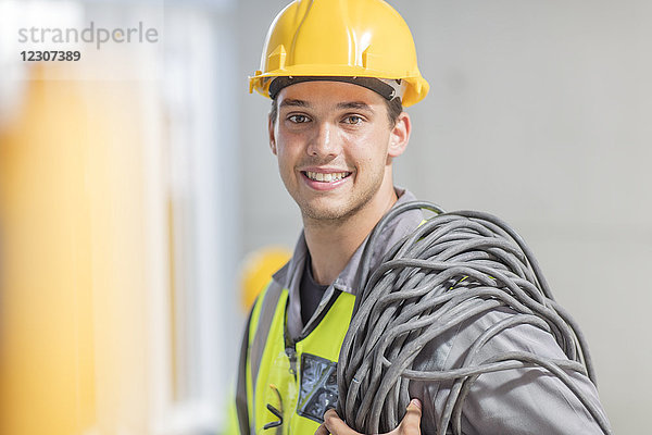 Porträt des lächelnden Elektrikers mit Kabel auf der Baustelle