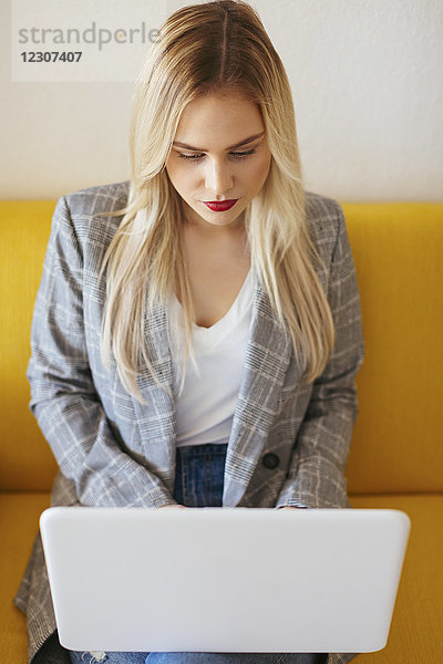 Geschäftsfrau auf gelber Couch sitzend  mit Laptop