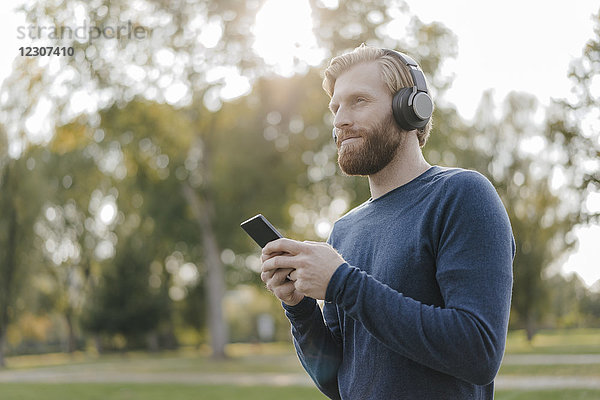 Mann hört Musik mit Kopfhörer und Smartphone im Park