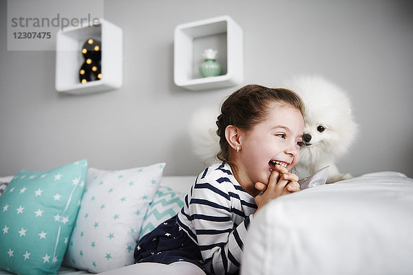 Lachendes kleines Mädchen spielt mit Hund auf der Couch im Wohnzimmer