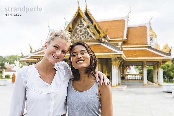 Thailand  Bangkok  Porträt von zwei lächelnden Freunden vor dem Tempel