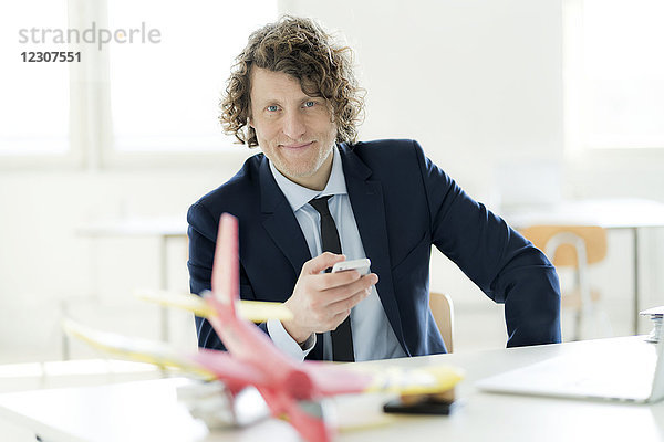 Geschäftsmann mit Smartphone  Spielzeugflugzeug auf seinem Schreibtisch