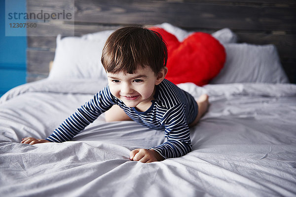 Porträt eines lächelnden Kleinkindes auf dem Bett kauernd