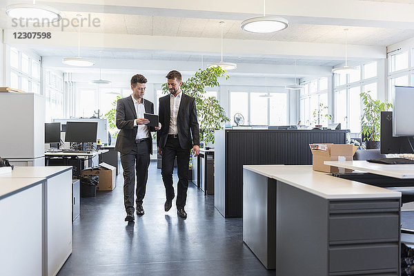Zwei Geschäftsleute  die im Büro spazieren gehen  digitale Tabletts benutzen  reden.