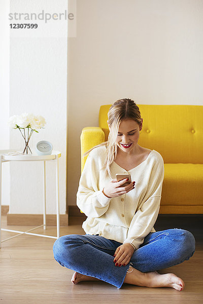 Blonde Frau mit Smartphone zu Hause