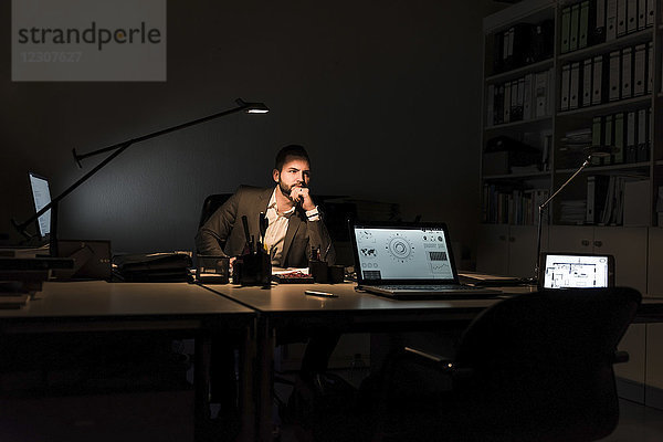 Nachdenklicher Geschäftsmann sitzt nachts am Schreibtisch im Büro.