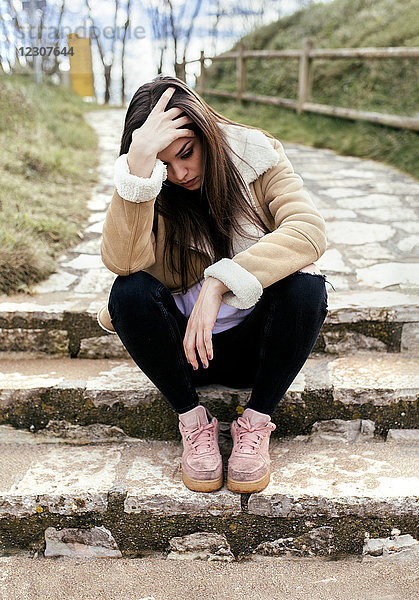 Traurige junge Frau im Freien auf einer Treppe sitzend