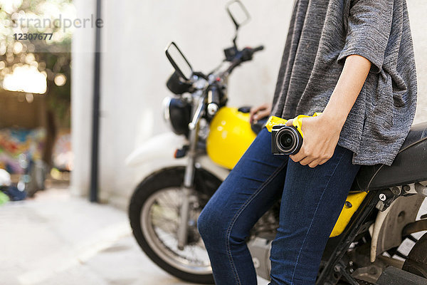 Nahaufnahme einer Frau mit an das Motorrad gelehnter Kamera