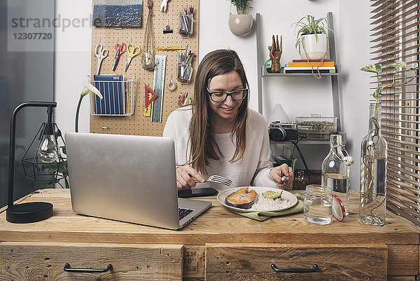 Frau beim Mittagessen am Holztisch mit Laptop