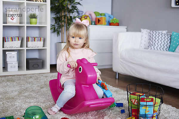 Porträt des kleinen Mädchens auf rosa Schaukelpferd im Wohnzimmer