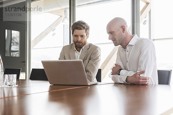 Zwei Geschäftsleute teilen sich den Laptop im Konferenzraum