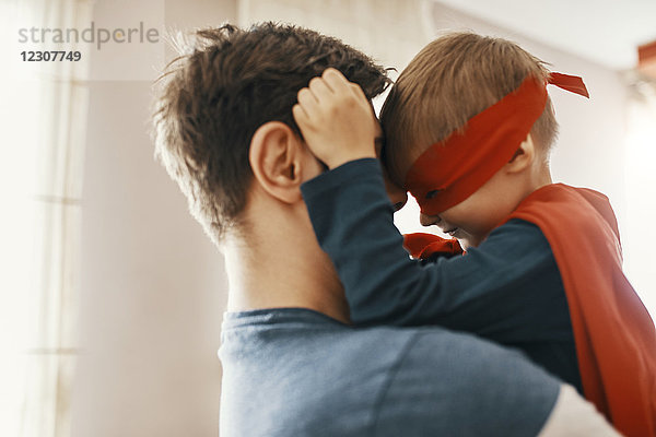 Kleiner Junge verkleidet als Superheld auf den Armen seines Vaters.